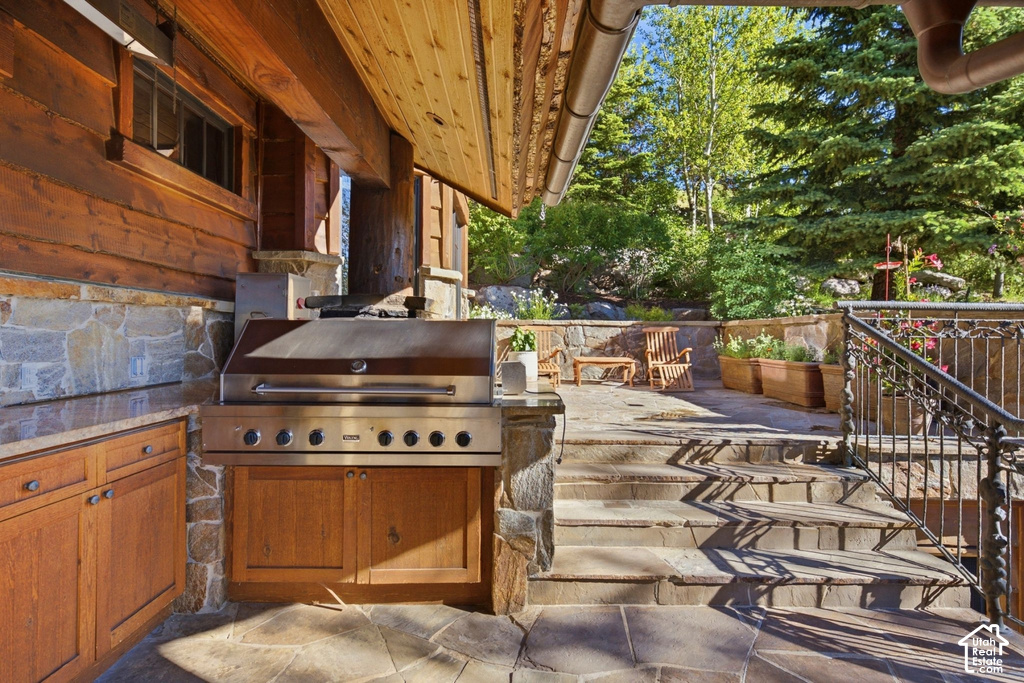 Outdoor kitchen featuring a stainless steel grill, wood cabinetry, and stone countertop