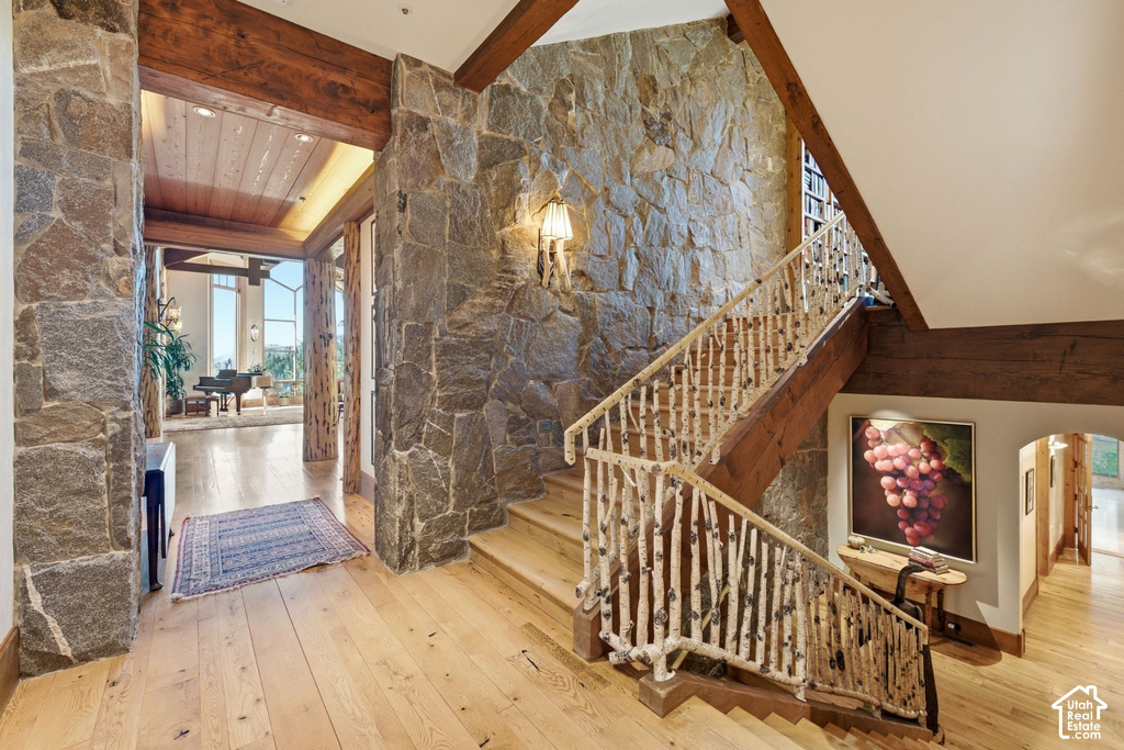 Stone-clad entryway featuring wood-finish flooring, exposed wood beams, and a natural branch staircase railing