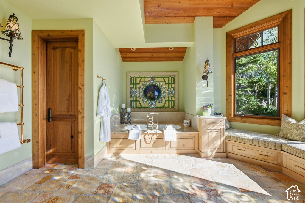 Bathroom featuring a built-in soaking tub, stone tile flooring, and a window seat with storage