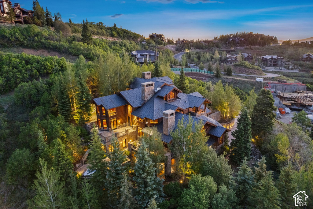 Hillside property featuring a multi-level structure with stone and wood siding, multiple chimneys, a dark shingle roof, and ample exterior lighting