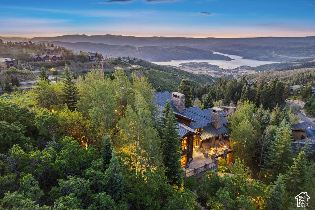 Hillside property featuring extensive tree coverage, a multi-level deck, stone chimneys, and a dark shingle roof