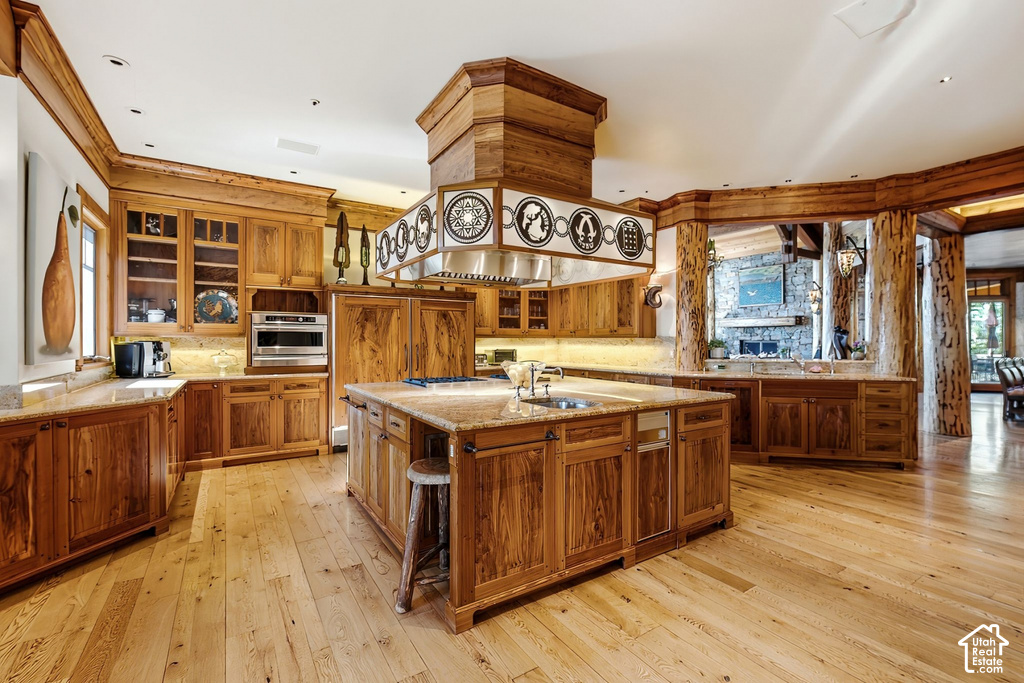 Gourmet kitchen with wood-finish flooring, extensive natural wood cabinetry, light-toned stone countertops, a large center island with integrated sink, and stainless steel appliances