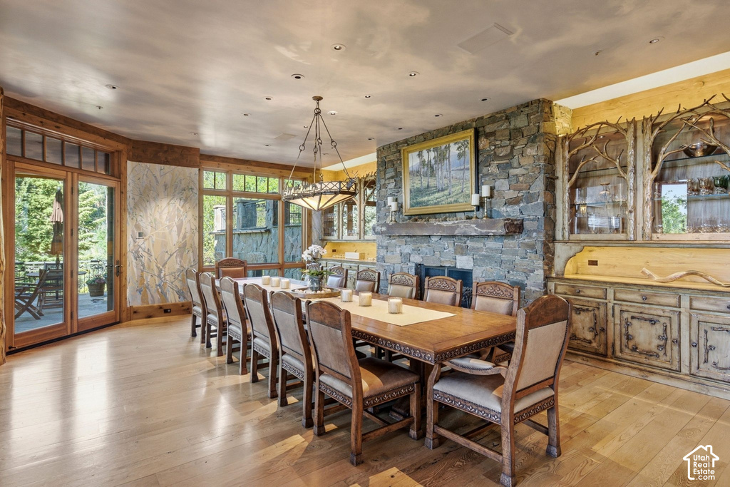 Spacious dining area featuring wood-finish flooring, a stone-clad fireplace with mantel, French doors opening to an outdoor patio, and custom built-in cabinetry with branch detailing