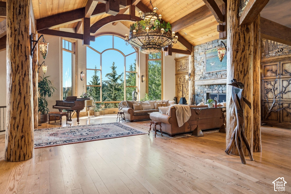 Grand living space featuring expansive arched windows, natural wood-finish flooring, exposed timber beams, a stone-clad fireplace, and rustic carved wooden doors