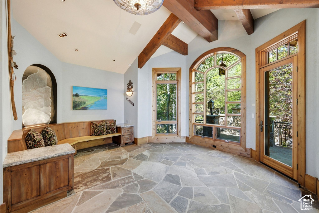 Spacious room featuring irregular flagstone flooring, exposed timber ceiling beams, an arched window with wooden framing, a wooden built-in bench, and a glass-paneled door