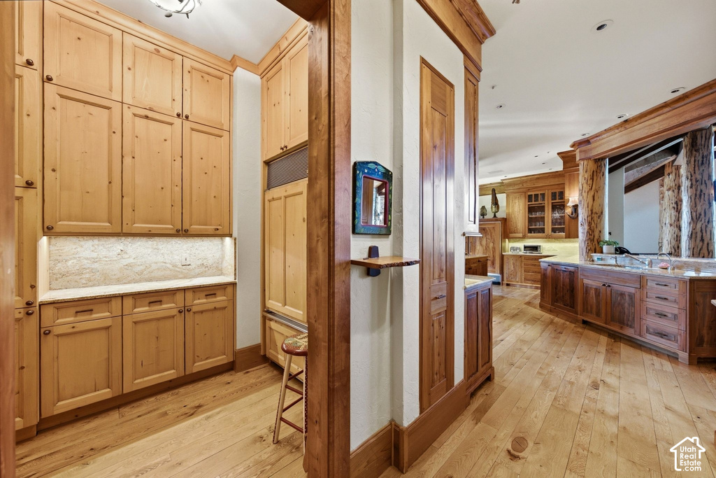 Custom wood cabinetry with under-cabinet lighting, natural wood-finish flooring, and a stone backsplash