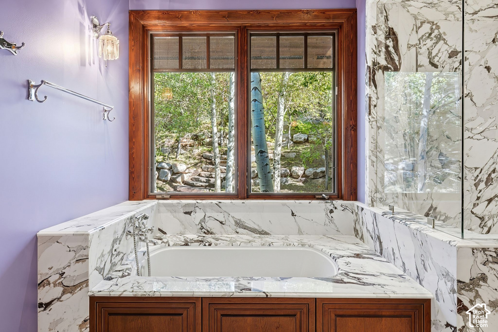 Built-in soaking tub with extensive marble surround, wood-frame window overlooking natural scenery, integrated shower partition, and wood-finish cabinetry