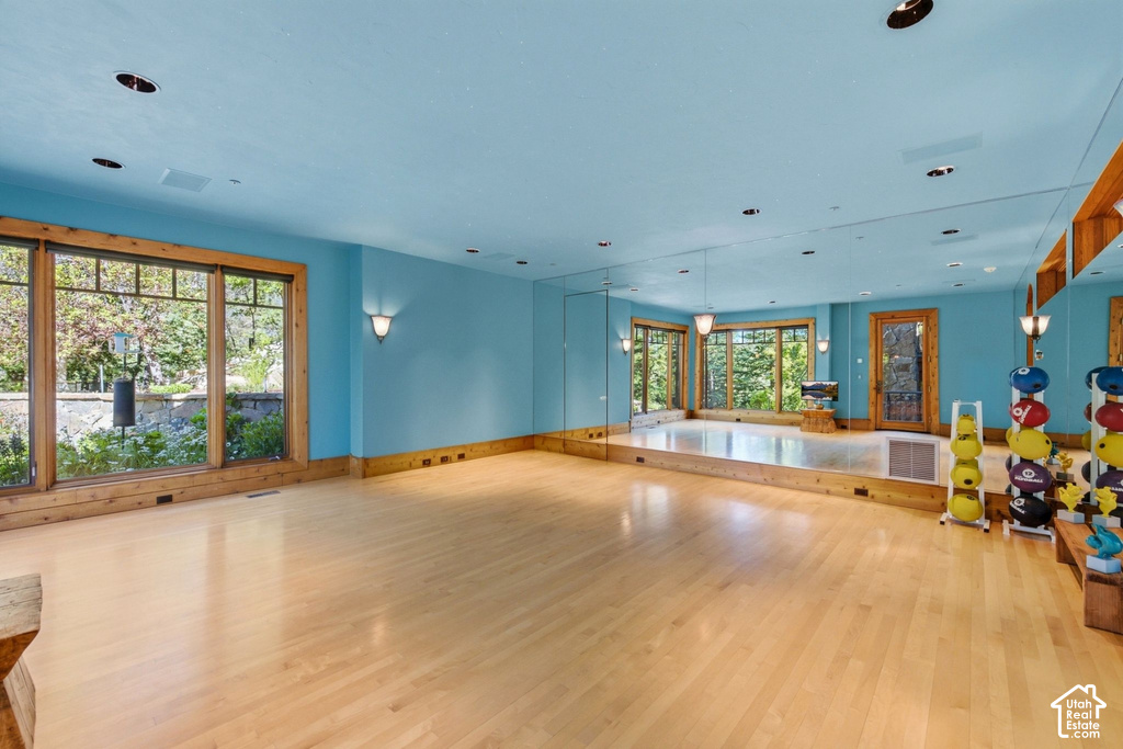 Spacious room featuring light wood-finish flooring, full-wall mirrors, and extensive natural light through large windows