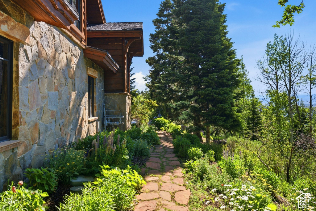 Stone facade with dark-framed windows and wood trim, featuring a flagstone pathway bordered by established landscaping
