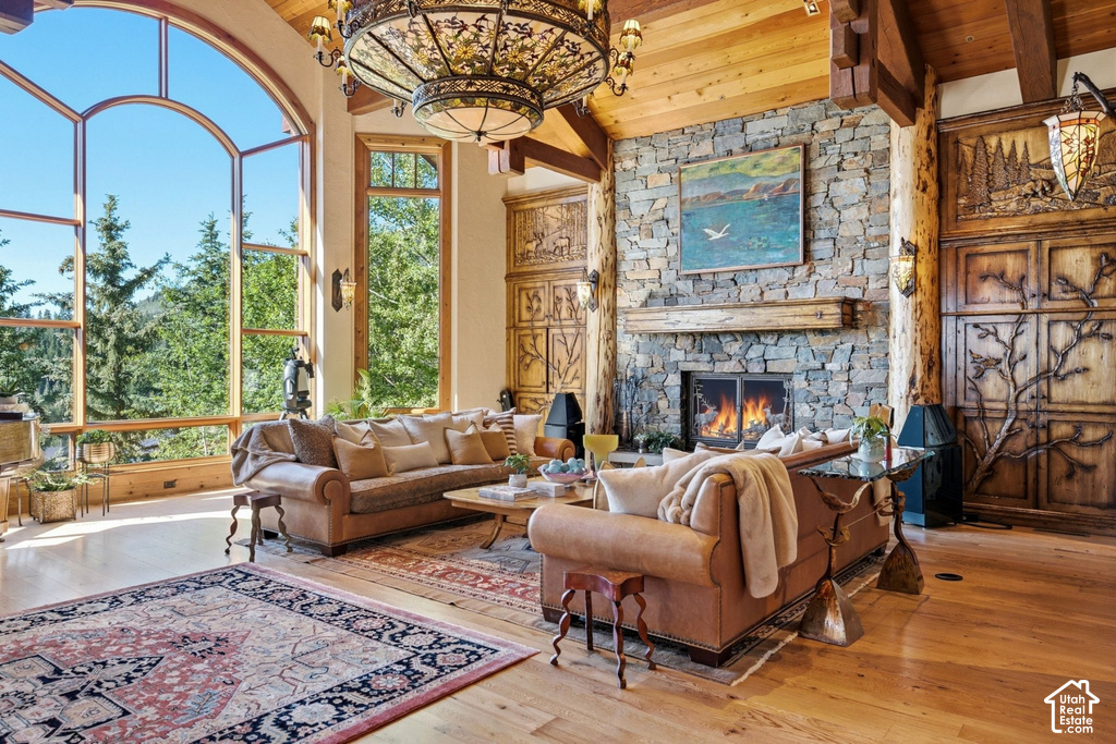 Great room featuring a floor-to-ceiling arched window, a stone fireplace with a wood mantle, wood-finish flooring, exposed wood beams, and built-in decorative wood panels