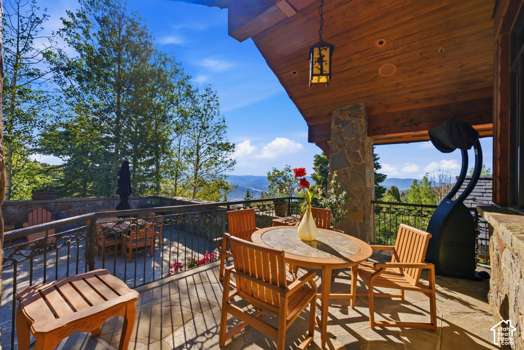Covered outdoor patio featuring stone column supports, a wood-paneled ceiling with an attached lantern fixture, and a durable stone-tiled floor