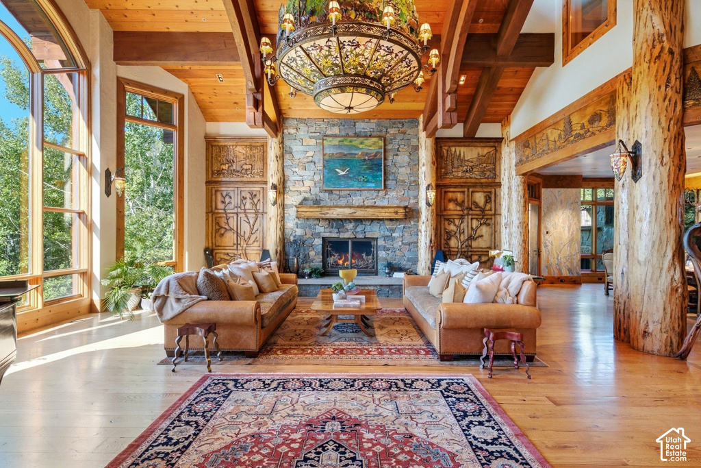 Spacious living area featuring a stone fireplace with a substantial wood mantel, exposed ceiling beams, wood-finish flooring, and expansive windows