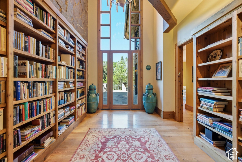 Double-height entry featuring extensive built-in wooden bookshelves, wood-finish flooring, a stone accent wall, and French doors with transom windows