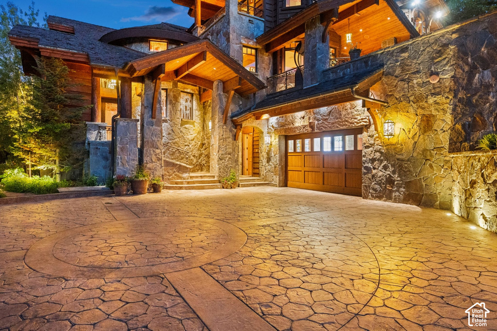 Stone-clad exterior featuring a wood garage door, stamped concrete driveway with circular detail, and exposed timber architectural elements