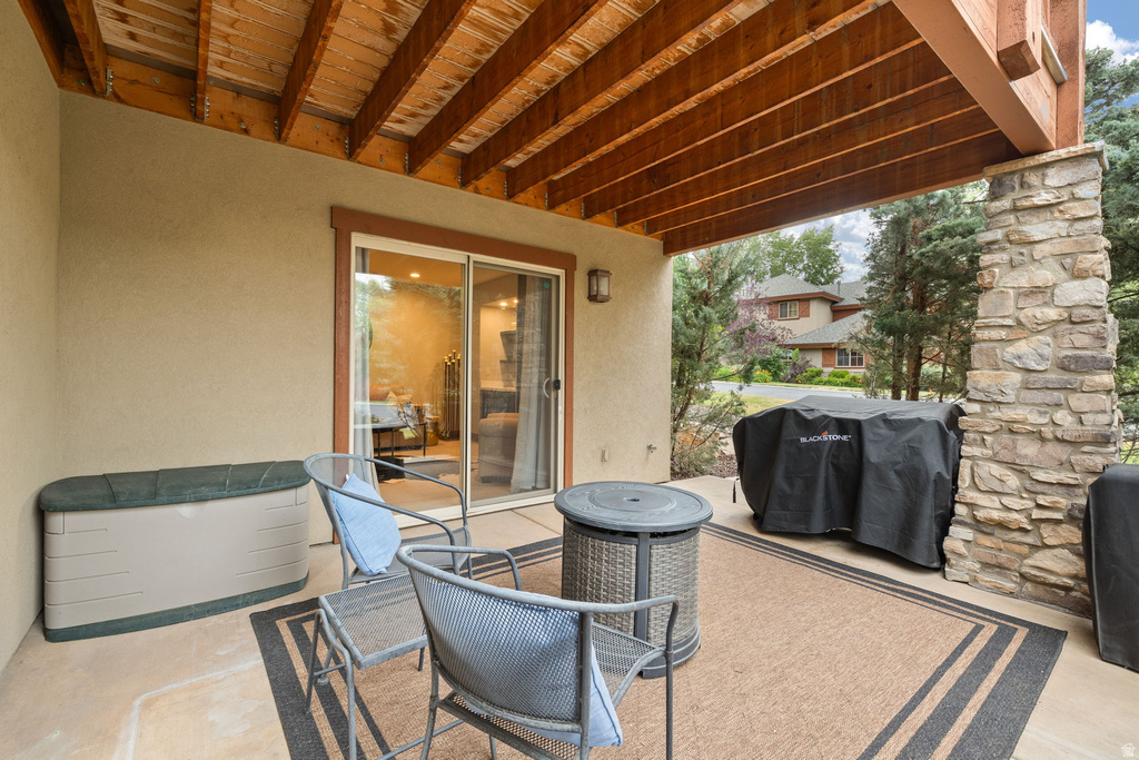Covered patio featuring a stone-clad column, wood-beamed ceiling, and a sliding glass door