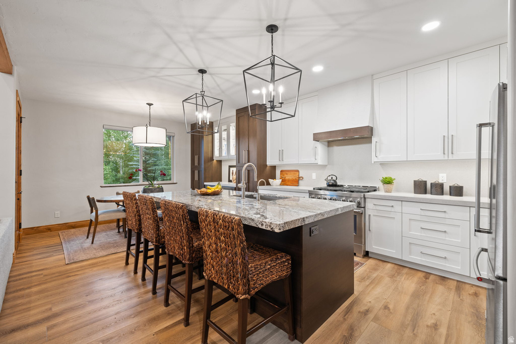Kitchen featuring a large central island with seating, granite countertops, stainless steel appliances, white upper and lower cabinetry, and wood-finish flooring