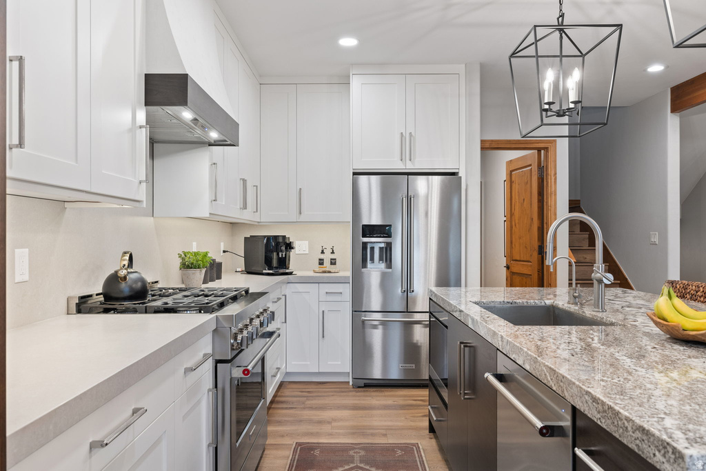 Kitchen featuring stainless steel appliances, a gas range with hood, white shaker cabinetry, an island with an undermount sink, and wood-finish flooring