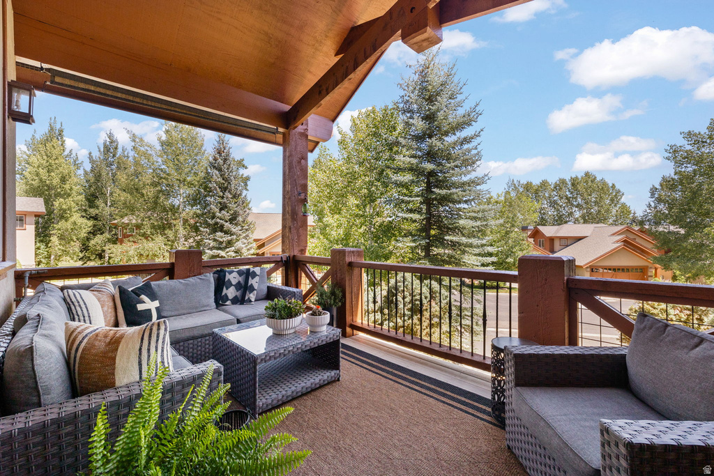 Covered outdoor balcony featuring exposed wood beams, wood railing with metal balusters, and a textured outdoor rug