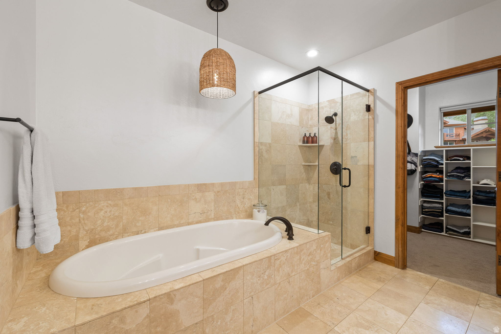 Soaking tub with surrounding stone tile, glass-enclosed shower with dark bronze fixtures, stone tile flooring, and a woven pendant light fixture