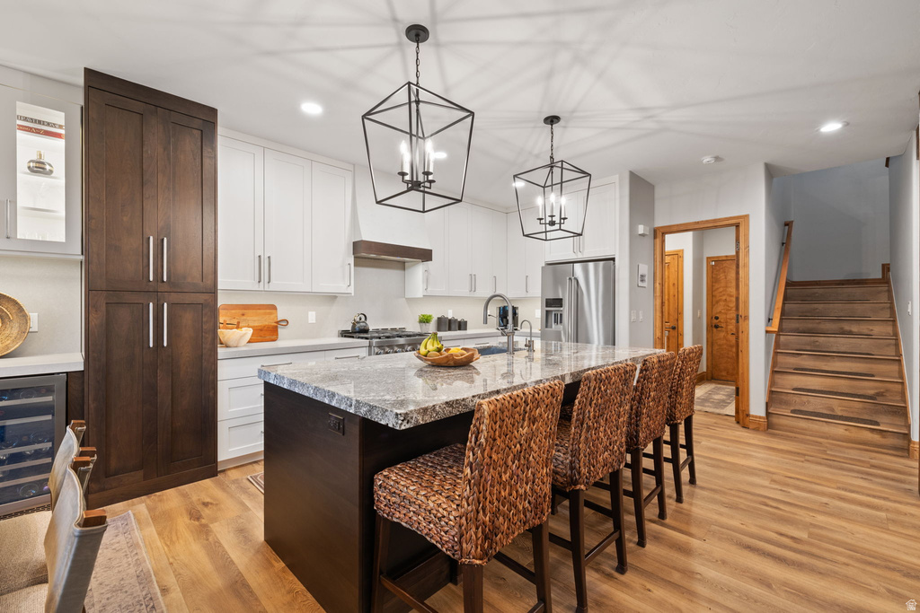 Kitchen featuring a central island with a stone countertop, white upper and lower cabinetry, dark wood-finish pantry storage, stainless steel appliances, and a built-in beverage cooler