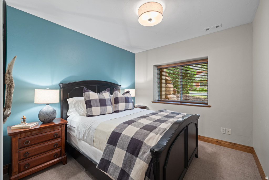 Bedroom featuring a contrasting accent wall, ceiling-mounted light fixture, recessed window with wood-finish trim, and carpet flooring