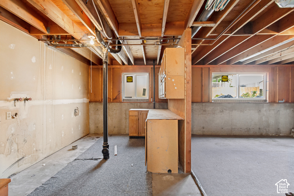 Unfinished basement featuring exposed wood joists, framed windows, concrete foundation walls, and existing cabinetry