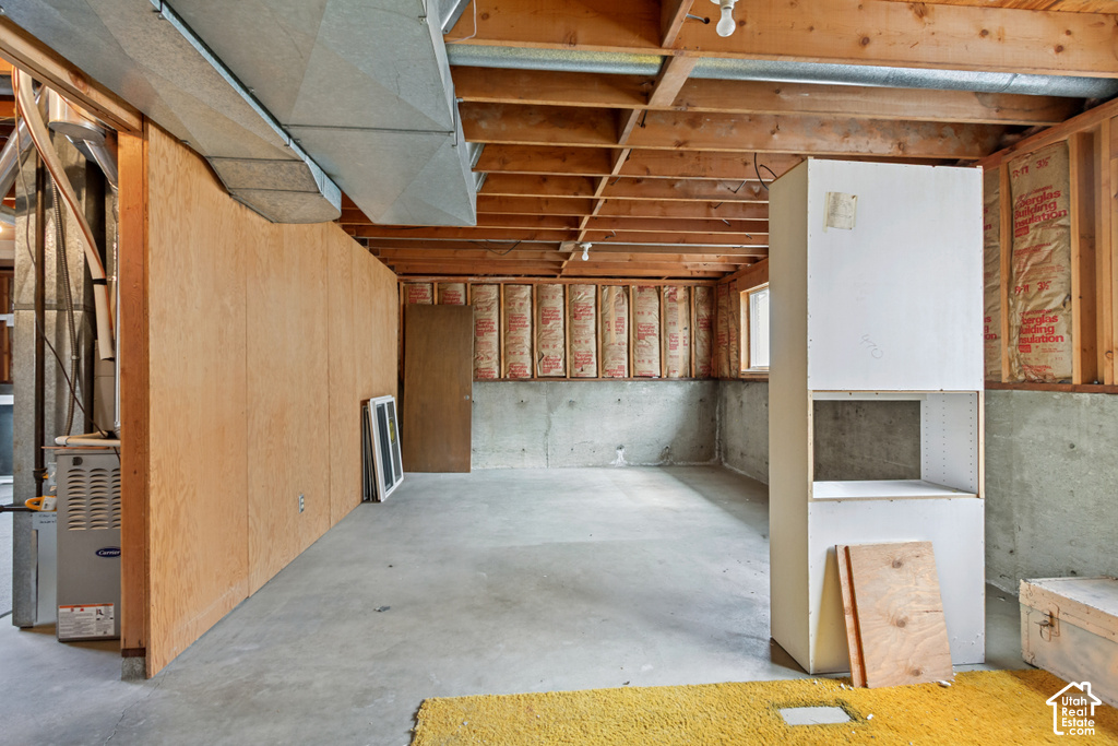 Expansive unfinished basement featuring concrete flooring, exposed ceiling joists, and a partial wood-paneled wall