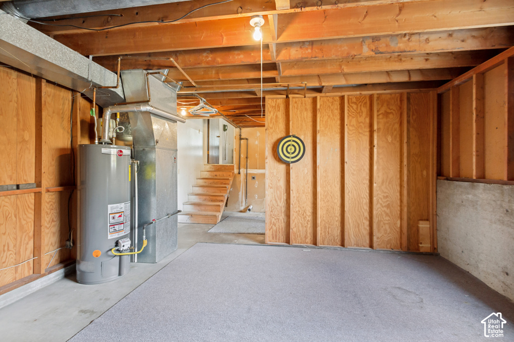 Lower-level space featuring exposed wood joists and structural beams, plywood wall paneling, and concrete flooring partially covered with gray carpet