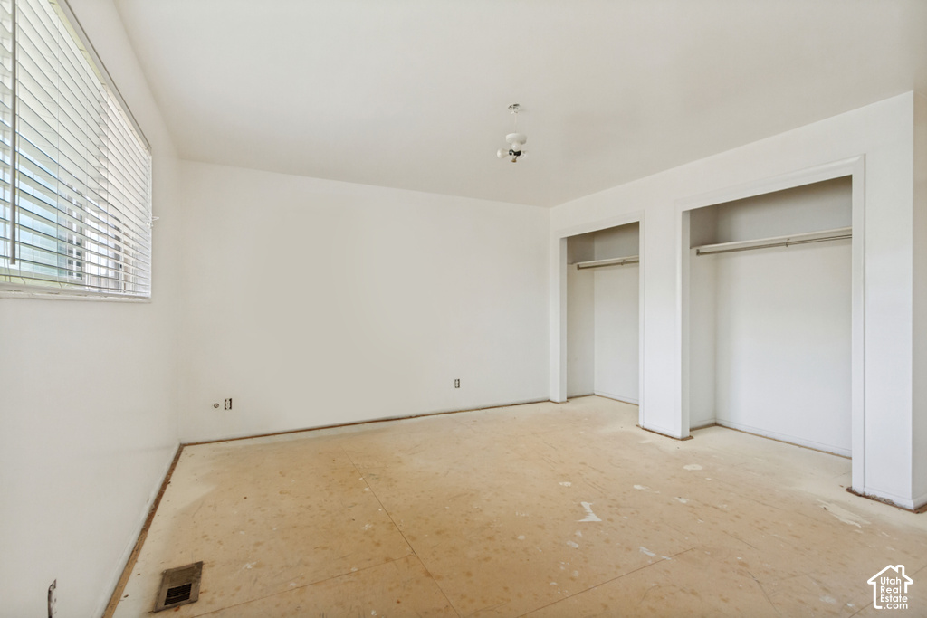 Spacious room featuring a large window with horizontal blinds, dual closet openings with hanging rods, a ceiling-mounted light fixture, and neutral wall tones