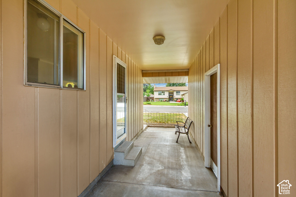 Covered porch with concrete flooring, vertical siding, an exterior light fixture, and a security screen door
