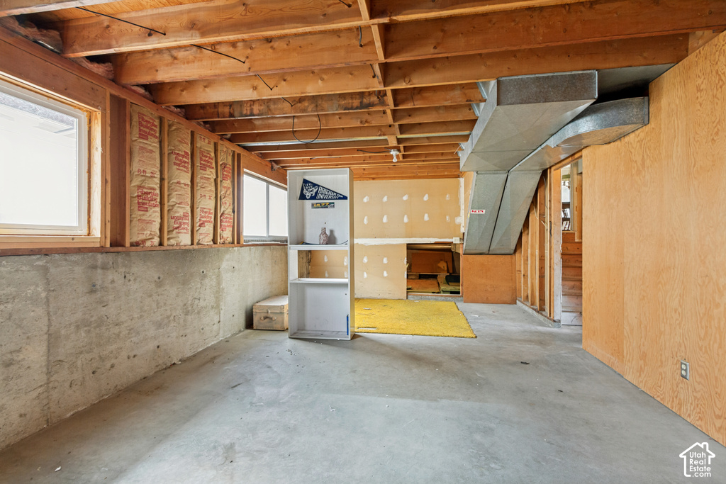 Unfinished basement area with exposed concrete flooring, wooden ceiling joists, and visible insulation in wall cavities