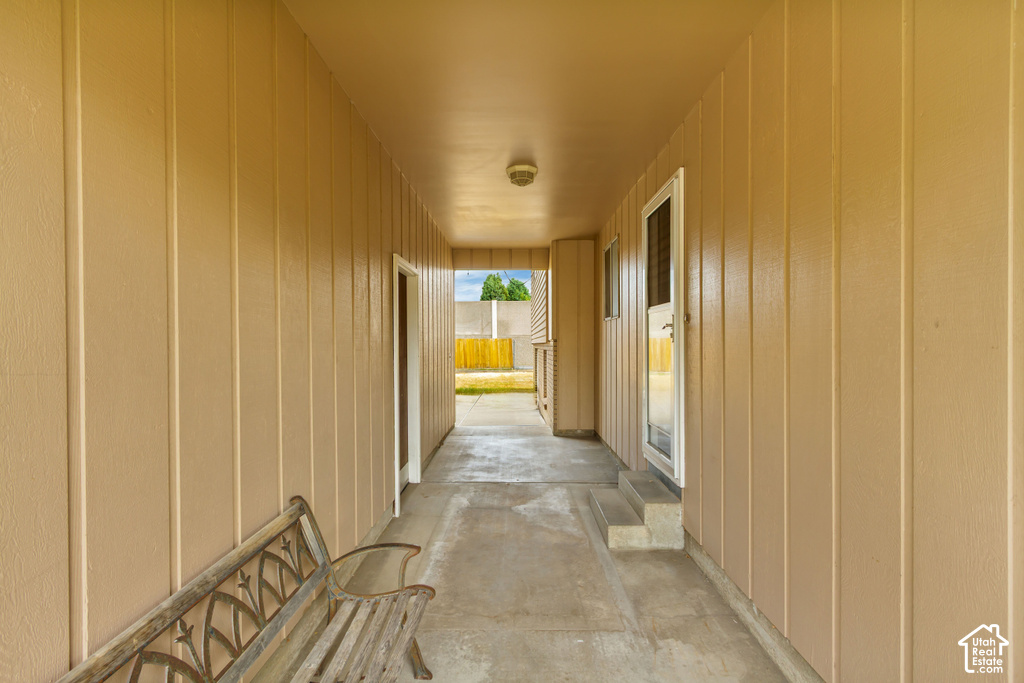 Covered breezeway featuring board and batten siding, a concrete pathway, exterior lighting, and an exterior door with steps