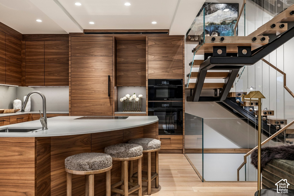 Modern kitchen featuring integrated wood-finish cabinetry, a curved island with a light-toned countertop, and a stainless steel gooseneck faucet