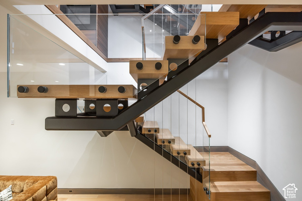 Open-tread staircase featuring wood steps, glass panel railings, and a black metal frame
