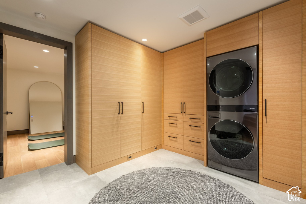 Laundry area featuring light wood-finish cabinetry, integrated stacked washer and dryer, and light-toned tile flooring