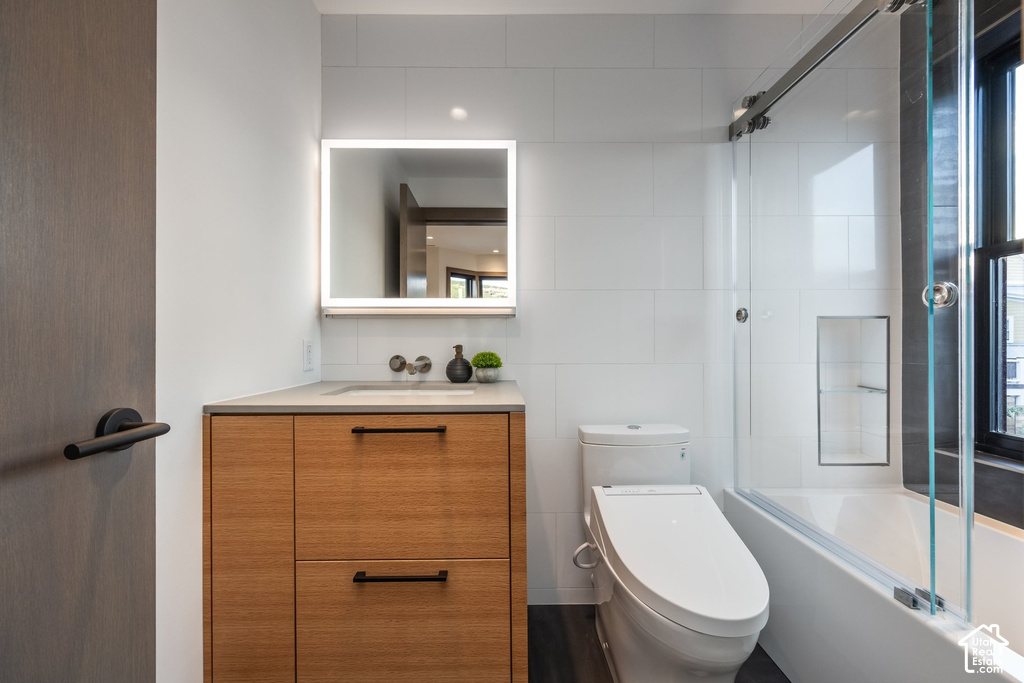 Contemporary bathroom featuring a light wood-finish vanity with dark pulls, a sleek countertop, and a backlit mirror