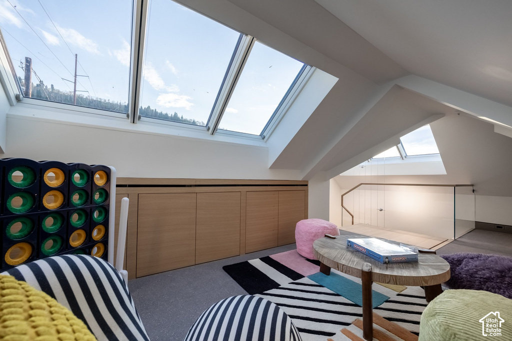 Attic space featuring multiple skylights, sloped ceilings, built-in blonde wood cabinetry, and a glass-paneled railing with a wood handrail