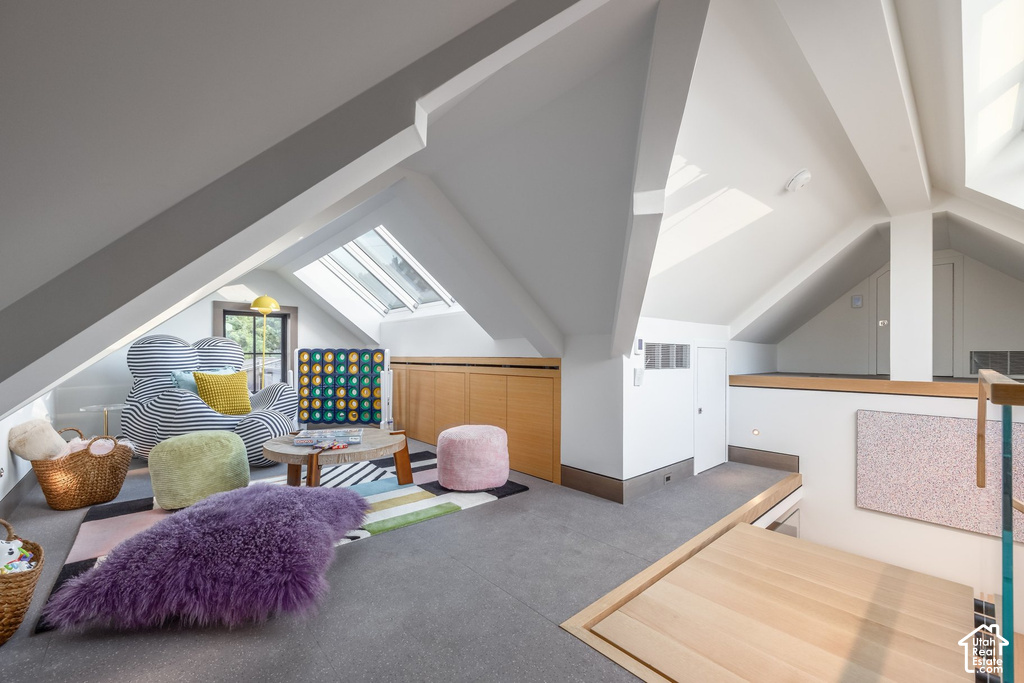 Attic space featuring vaulted ceilings with exposed beams, multiple skylights, built-in wooden cabinetry, and light gray flooring