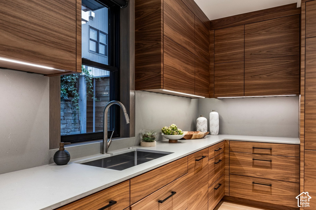 Contemporary kitchen featuring wood-finish cabinetry with integrated lighting, light-toned countertops, and a double basin stainless steel sink with a gooseneck faucet