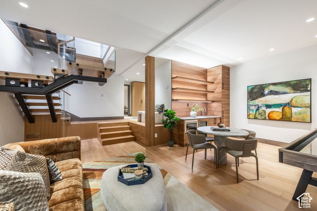 Open-concept living area featuring a contemporary floating staircase with glass railings, wood-finish flooring, a built-in wet bar with integrated shelving, and recessed lighting