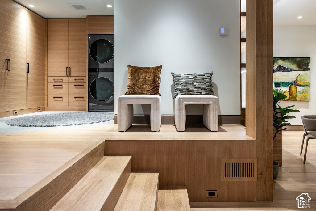 Integrated laundry area with stacked appliances, extensive light wood cabinetry, and a concrete-finish floor
