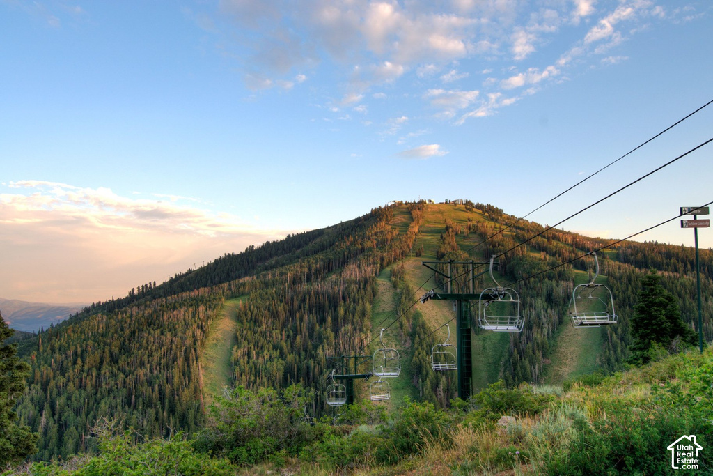 Mountain landscape featuring ski lift infrastructure, forested slopes, and distant mountain ranges under a partly cloudy sky