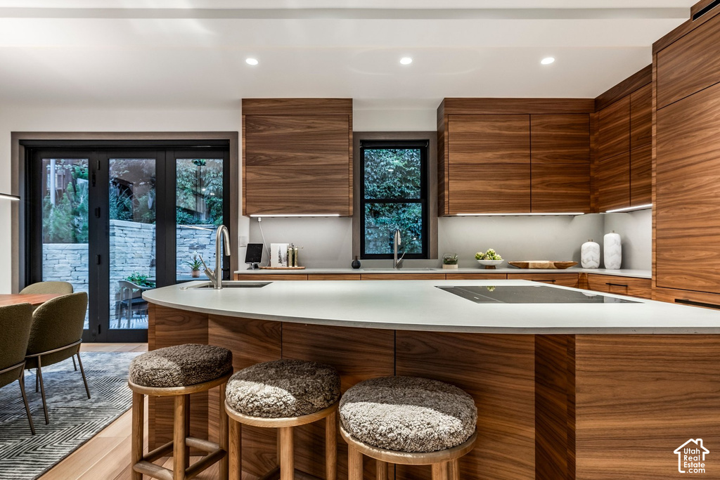 Modern kitchen featuring wood-grain cabinetry, a curved island with integrated cooktop, a stainless steel sink, and recessed lighting