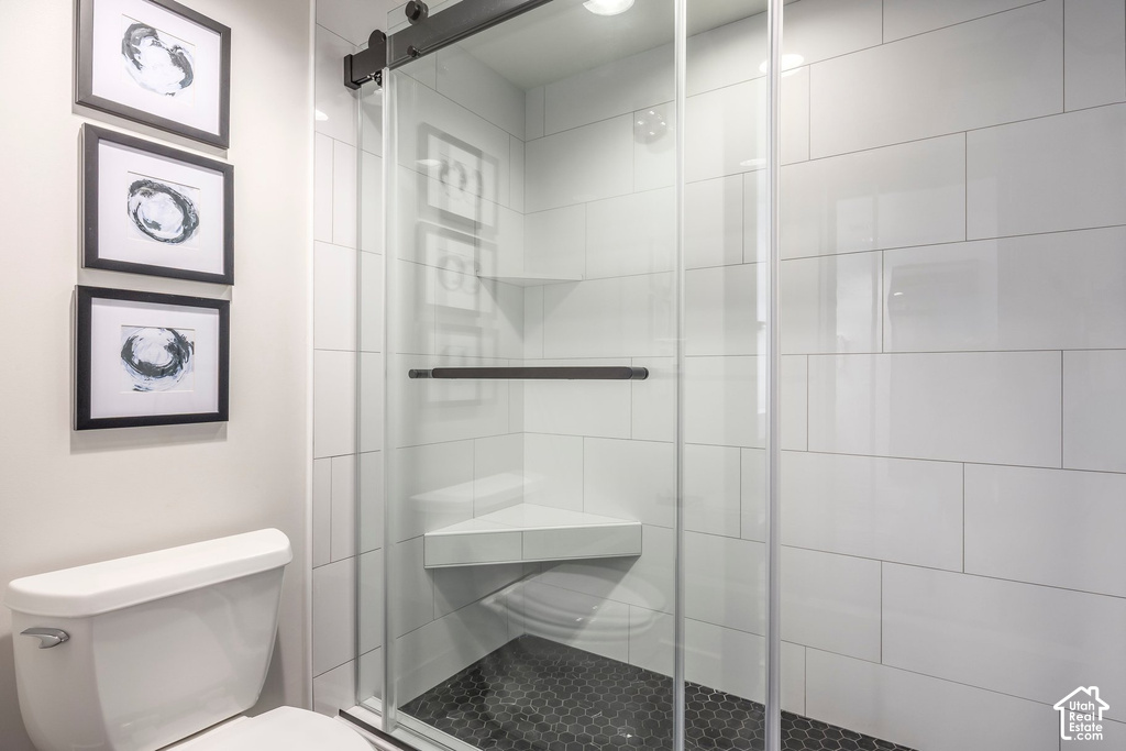 Glass-enclosed shower featuring a sliding door with dark-finish hardware, white subway tile surround, dark hexagonal tile flooring, and a built-in shower bench