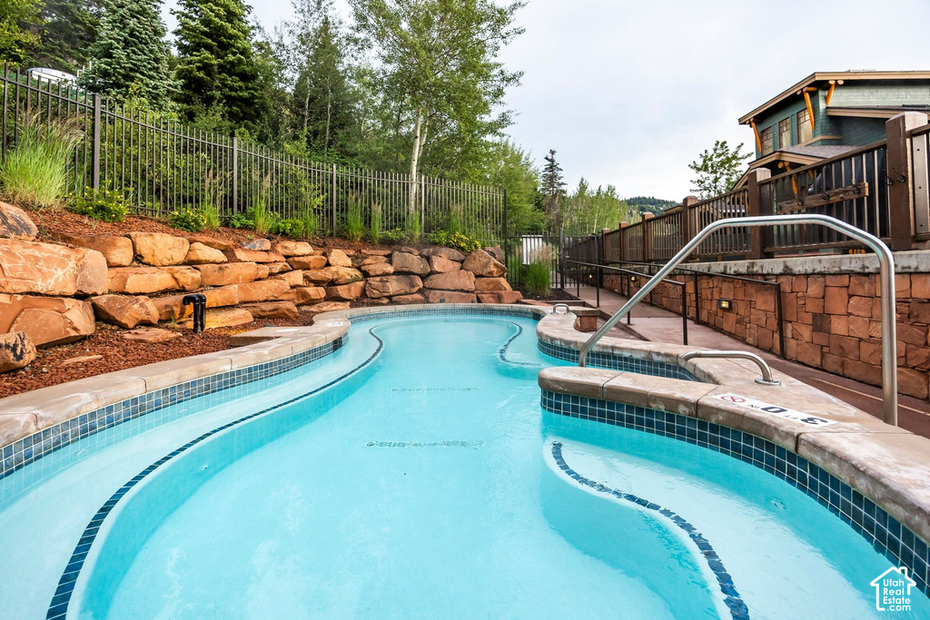 Curved multi-depth pool with mosaic tile trim, integrated handrails, and surrounding stone hardscaping