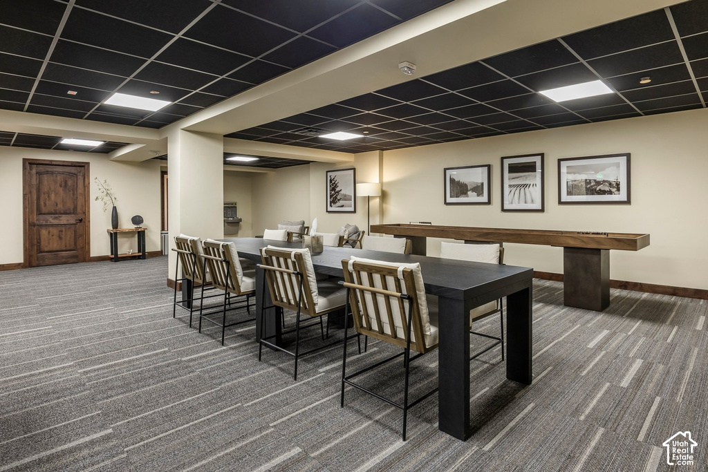 Spacious common area featuring textured carpet flooring, a dark grid ceiling, and recessed lighting