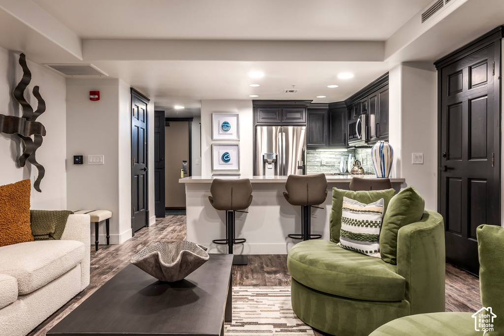 Open-concept living area featuring wood-finish flooring, a kitchen with dark cabinetry, stainless steel appliances, a light-toned countertop, and recessed lighting