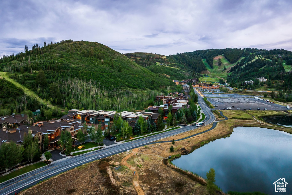 Expansive mountain landscape featuring a dark blue lake, a winding road, and multi-story residential buildings