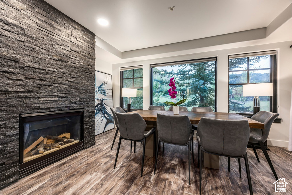 Dining area featuring a stacked stone fireplace with a black surround, wood-finish flooring, and large windows with black frames