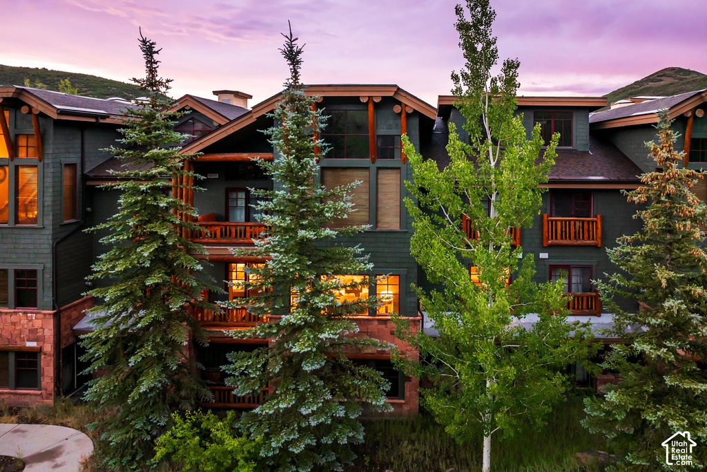 Multi-story structure featuring dark green siding, wood-finish trim, multiple balconies with wood railings, and stone accent walls